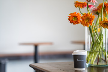Cup coffee on wooden table next to Gerbera vase
