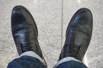 black men's autumn boots with laces and brogues, black shoes with jeans. Against the background of light gray tile floor. loneliness, alone