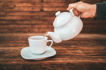 Tea time, brewing and pouring tea, cup of freshly brewed tea, warm soft and light, with wooden background