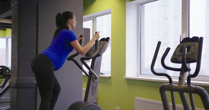 Pregnant young woman working out on stepper machine at the gym