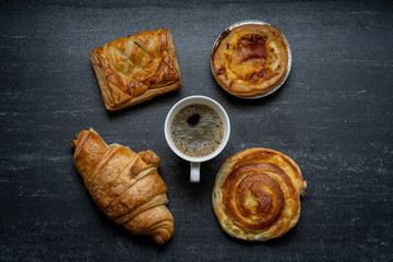 Cup coffee, croissant chicken pie on black background table.