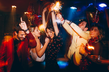 Group of friends having fun and holding sparklers at New Year's party - obrazy, fototapety, plakaty