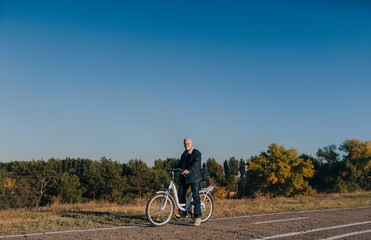 An elderly man, a pensioner rides an electric white bike on an asphalt road against the background...