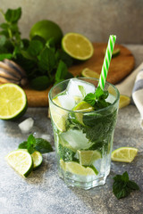 Fresh Mojito cocktail with lime, ice and mint in a glass on a gray stone background. Summer cold drink and cocktail.