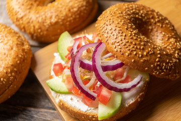 Sesame bagels with spreadable cream cheese and vegetables on wooden background