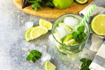 Fresh Mojito cocktail with lime, ice and mint in a glass on a gray stone background. Summer cold drink and cocktail.