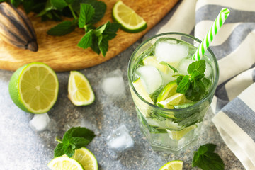 Fresh Mojito cocktail with lime, ice and mint in a glass on a gray stone background. Summer cold...