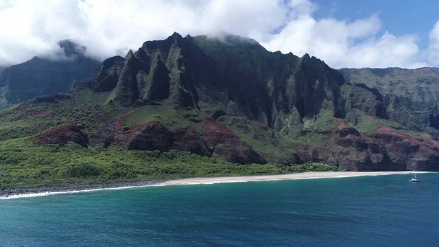 Wide aerial view of the Na pali coastline in Kauai, Hawaii. Drone pans across the scene with a catamaran in the distance.