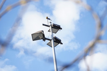modern lighting mast with lanterns on a background of blue sky with white clouds through the hole. Street Lights