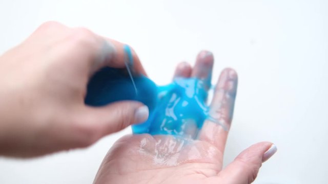 Girl stretching blue slime to the sides. Woman hands playing slime toy. Making slime on white. Trendy liquid toy sticks to hands and fingers. 4k footage.