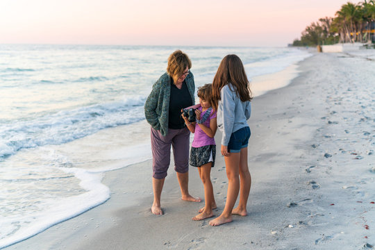 Grandmother with grandchildren on beach at sunset with camera