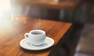 Espresso in white cup on wooden table in cafe.