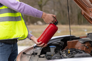 A man demonstrating how to use a fire extinguisher over a car engine