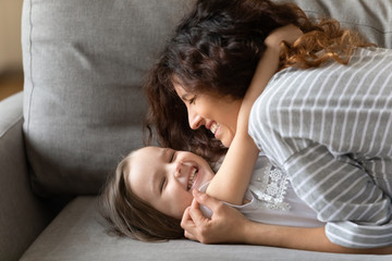 Closeup view happy mother cuddle preschool daughter lying on couch