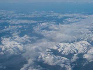 Aerial view of snow covered french and spanish pyrenees with snow covered mountains viewed from an aeroplane. Blue sky white clouds background
