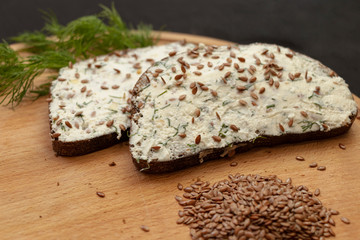 Healthy sandwich. Rye bread with salty white cheese and flaxseed. Board. Black background.