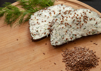 Fototapeta premium Healthy sandwich. Rye bread with salty white cheese and flaxseed. Board. Black background.