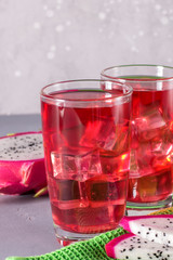 Glass of mango dragonfruit refresher drink on grey table with ice cubes. Copy space.