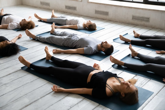 Young people meditating in Savasana pose, practicing yoga at lesson