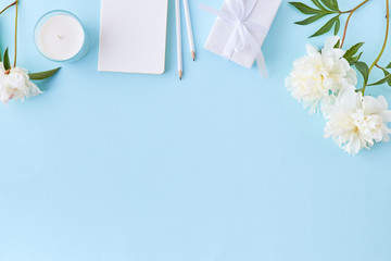 Flat lay blogger or freelancer workspace with a notebook and white peonies on a blue background