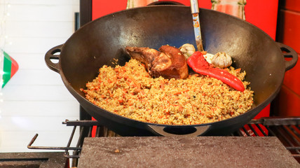 Delicious Uzbek pilaf in a cauldron in the open air at a street food festival. Cooking rice with meat and vegetables. A large pot of national Kazakh cuisine on the street during the festival.