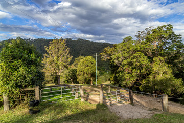 Fototapeta na wymiar Rural property in Australia, gate leads to dirt tracks and woodlands large tree covered hill in the distance