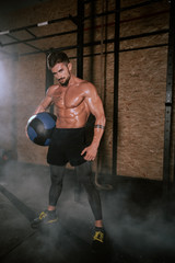 Details of a athletic guy using a cross fit ball to do his hard training workout exercises in a dark gym class