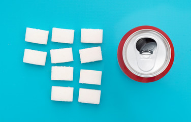 Unhealthy food concept - sugar in carbonated drinks. Sugar cubes and fizzy cola drink can. Flat...