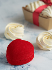 Red casket for a ring or a gift on a gray table. Homemade marshmallows (zephyr) on the table. Homemade sweets. Vertical orientation. Selective focus on the box.