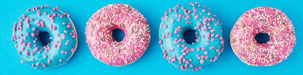 Different types of a colorful donats decorated sprinkles and icing on blue background, long banner