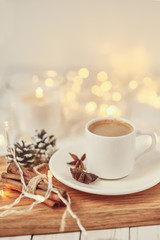 Fototapeta na wymiar Cup of coffee with a garland lights and decoration on table. Cozy home concept