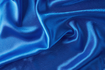 Blue silk background with a folds.  Abstract texture of rippled satin surface