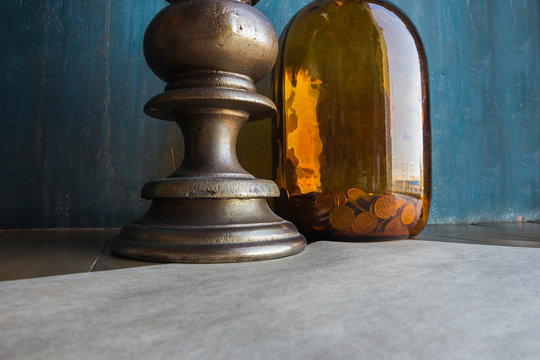 Big Brown Glass Jar With Coins And Massive Candleholder With White Candle On It On Blue Shabby Wall Background, Concept Of Savings, Trading, Savings Or Electricity Economy