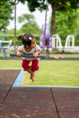 Cute little asian girl playing swing at playground.