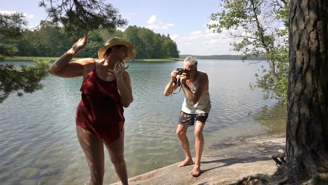 Elderly man taking picture of attractive senior woman with vintage camera on the beach. Funny active loving elderly couple carefree and happy together on vacation in Northern Europe, Finland