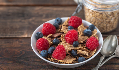 Healthy breakfast of granola chips with blueberries and strawberries on dark desk.