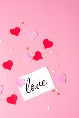 Valentines day. A postcard with the inscription love, pink, red and white hearts on a pink background. Copy space, top view