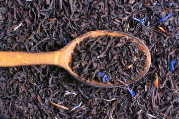 A wooden spoon of black tea with blue petals.