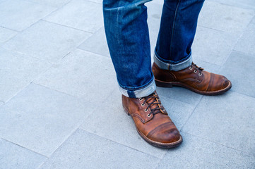 Young man fashion legs wearing blue jeans and brown boots on the tile floor.