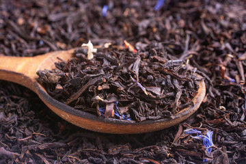 A wooden spoon of black tea with blue petals.
