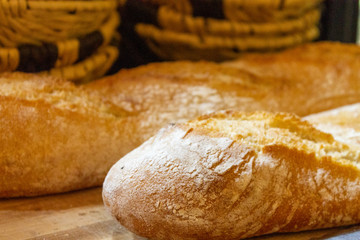 homemade bread placed on wood to cut with baskets behind.