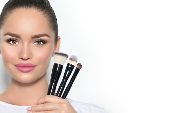 Beauty model girl, makeup artist holding set of make up brushes and smiling. Beautiful brunette young woman with perfect skin and nude make-up. Perfect skin closeup. Face contouring makeup. On white.