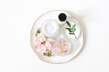 Styled beauty composition. Skin cream, shampoo bottle, rose flowers and Himalayan salt. White table...