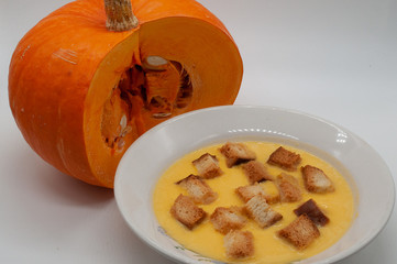 pumpkin soup with breadcrumbs in a white plate and pumpkin in the background