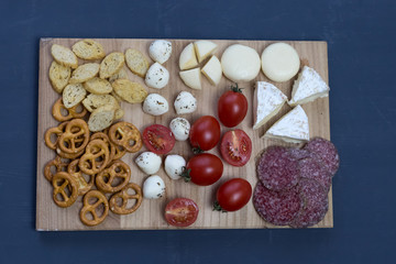  snacks, cheese, vegetables lie on a wooden board on a blue background