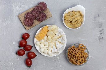  cheese, snacks, tomatoes lie on a plate and board on a gray background