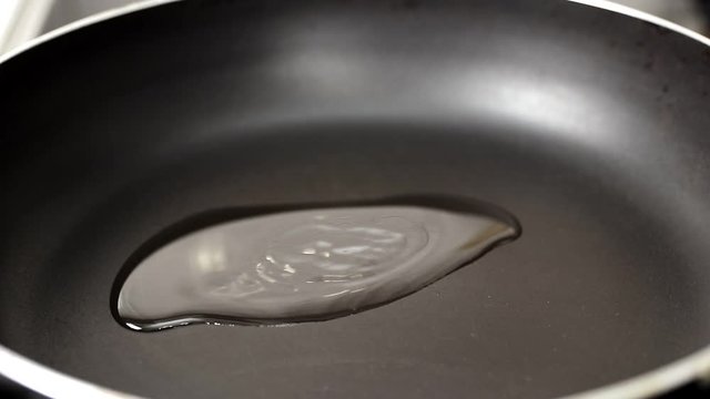 hand pouring olive oil into a black hot pan, liquid spreading over a dark surface