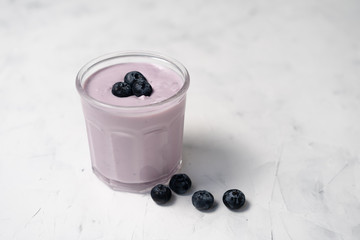 Fototapeta na wymiar Tasty fresh blueberry yoghurt shake dessert in glass standing on white table background.