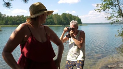 Elderly man taking picture of attractive senior woman with vintage camera on the beach. Funny active loving elderly couple carefree and happy together on vacation in Northern Europe, Finland - Powered by Adobe
