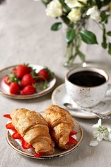 Breakfast in French. Croissant sandwich with I soft cheese and strawberries. And black coffee, a bouquet of flowers. Fresh strawberries. Soft focus. Space for text.  Copy Space